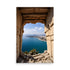 Ornate stone archway frames Mediterranean city. Carved arch unveils vibrant cityscape view. Turquoise sea meets horizon beyond curved coastline.